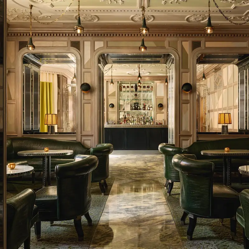 An elegant bar with dark green leather seating, marble floors, mirrored panels, and soft lighting, creating a refined, intimate ambiance.