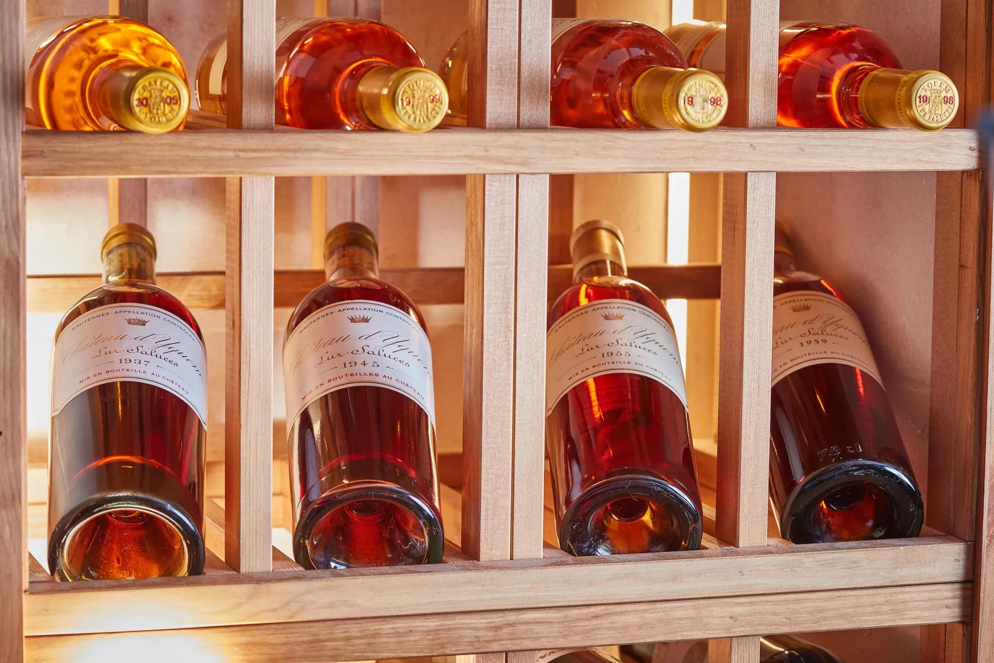 Rosé wine bottles stored horizontally in a wooden rack, softly lit to highlight amber tones and labels.