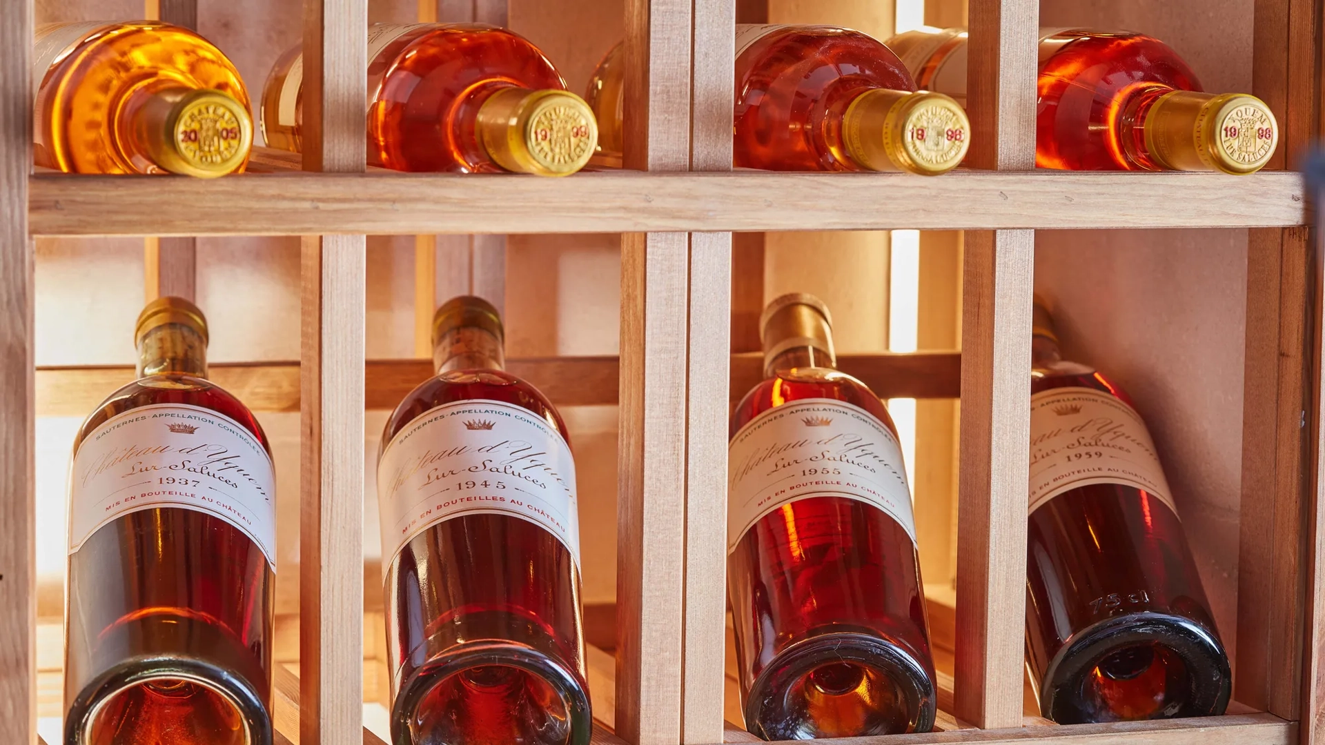 Rosé wine bottles stored horizontally in a wooden rack, softly lit to highlight amber tones and labels.