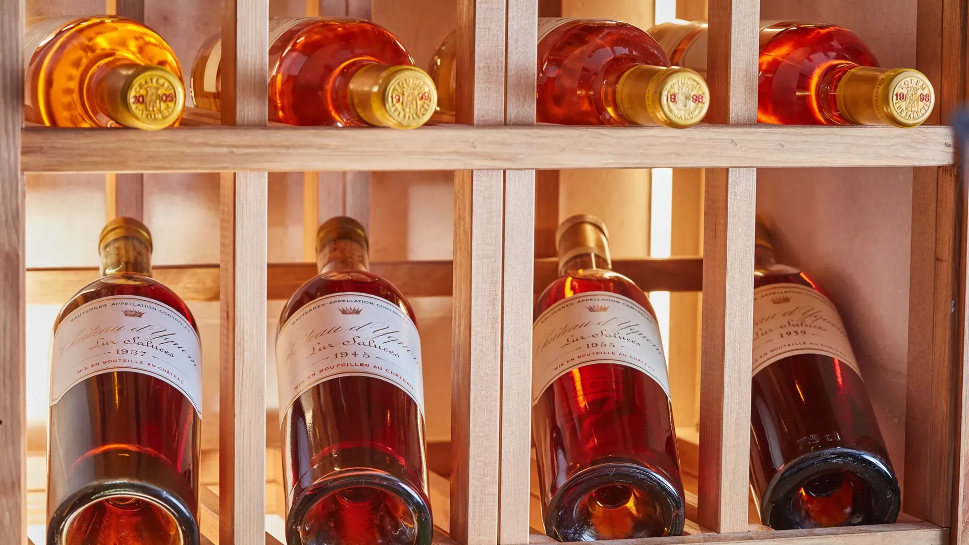 Rosé wine bottles stored horizontally in a wooden rack, softly lit to highlight amber tones and labels.