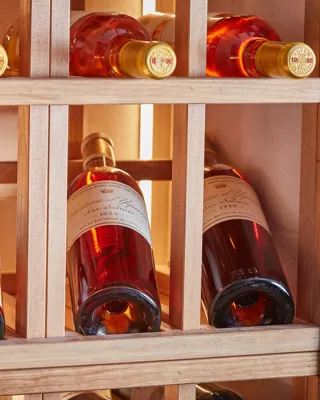 Rosé wine bottles stored horizontally in a wooden rack, softly lit to highlight amber tones and labels.