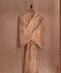 A floral kimono in soft peach and gold tones hangs on a wooden wall hook beside a light wood counter and minimalist sink at The Maybourne Riviera.