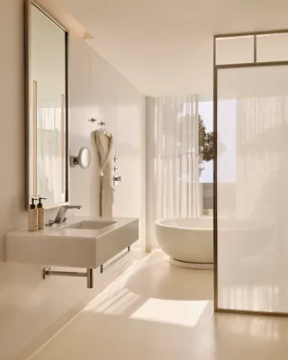 Salle de bain élégante avec un lavabo moderne, un miroir éclairé et une baignoire ovale indépendante près de rideaux légers et d’une fenêtre donnant sur des arbres.
