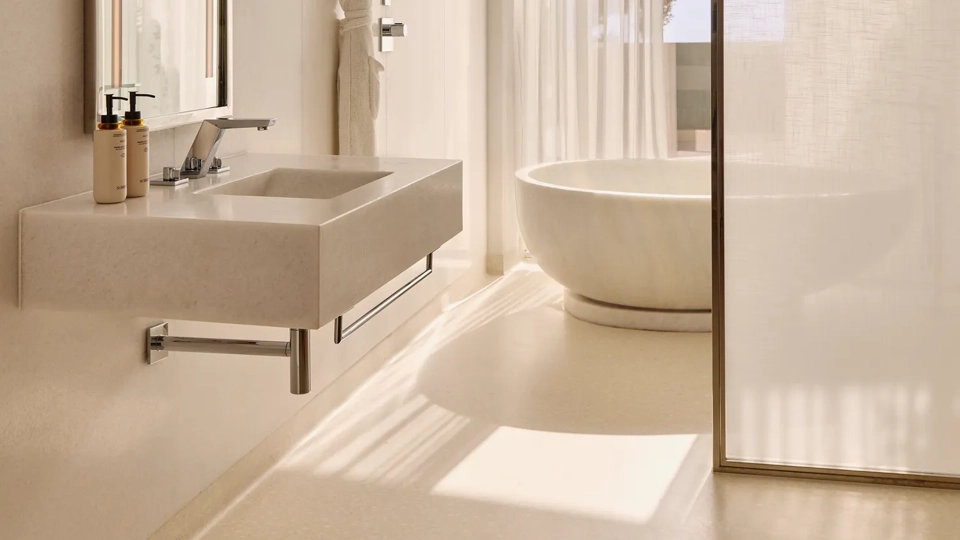 Salle de bain élégante avec un lavabo moderne, un miroir éclairé et une baignoire ovale indépendante près de rideaux légers et d’une fenêtre donnant sur des arbres.