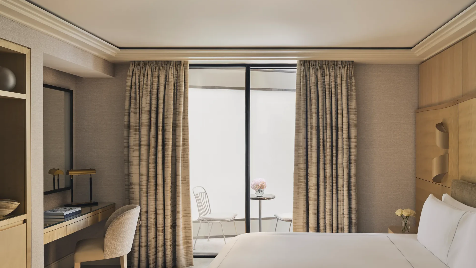 Serene bedroom with desk, king bed, and private courtyard terrace with two white chairs and a marble table.