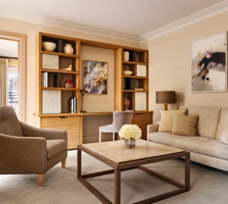 Bright living room with a neutral sofa, armchair, and a wooden desk built into shelving, decorated with abstract artwork and ceramic vases.