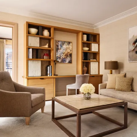 Bright living room with a neutral sofa, armchair, and a wooden desk built into shelving, decorated with abstract artwork and ceramic vases.