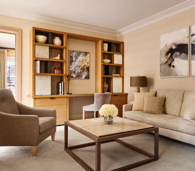 Bright living room with a neutral sofa, armchair, and a wooden desk built into shelving, decorated with abstract artwork and ceramic vases.