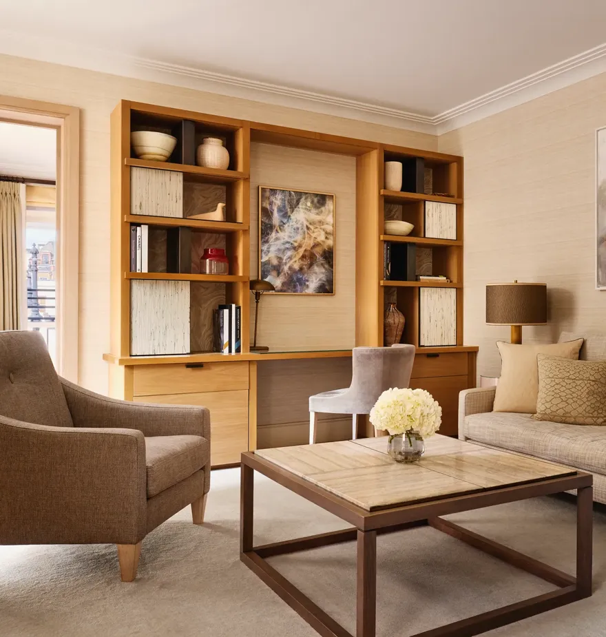 Bright living room with a neutral sofa, armchair, and a wooden desk built into shelving, decorated with abstract artwork and ceramic vases.