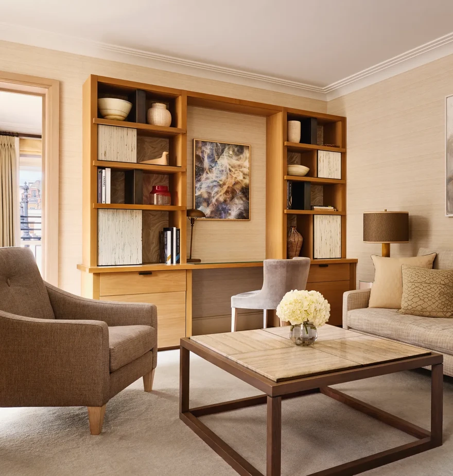 Bright living room with a neutral sofa, armchair, and a wooden desk built into shelving, decorated with abstract artwork and ceramic vases.