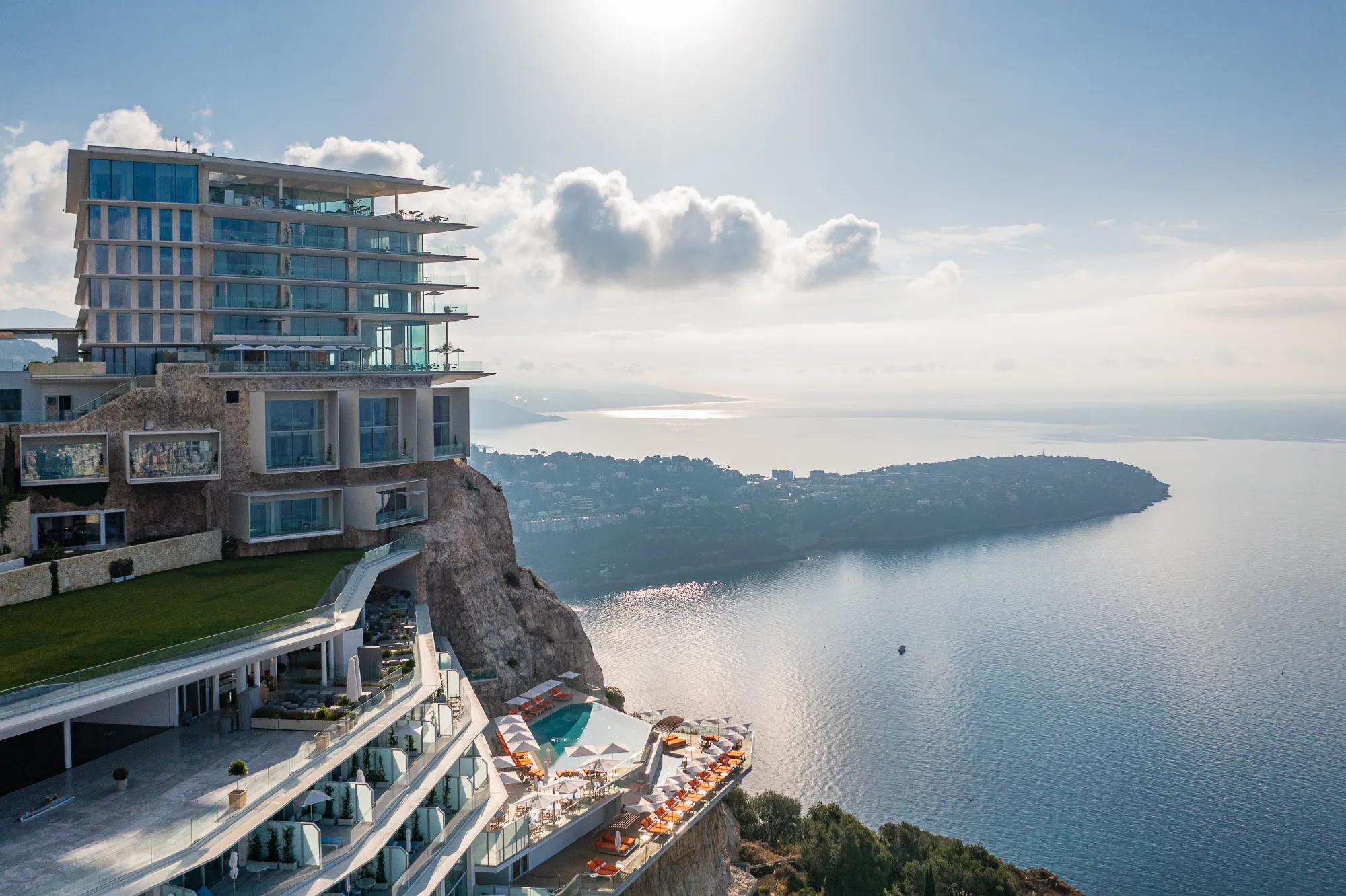 Hôtel perché sur une falaise avec terrasses, piscine extérieure et vue panoramique sur la mer et la côte.