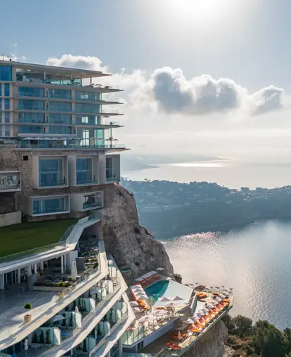 Hôtel perché sur une falaise avec terrasses, piscine extérieure et vue panoramique sur la mer et la côte.