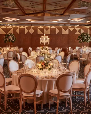 Grand ballroom with round tables, tall floral arrangements, candelabras, and warm ambient lighting.