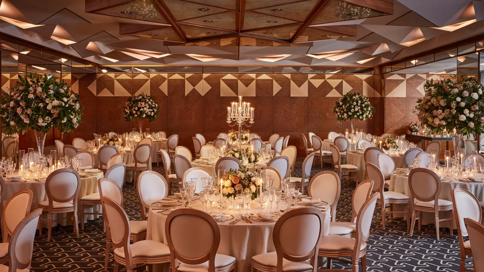 Grand ballroom with round tables, tall floral arrangements, candelabras, and warm ambient lighting.