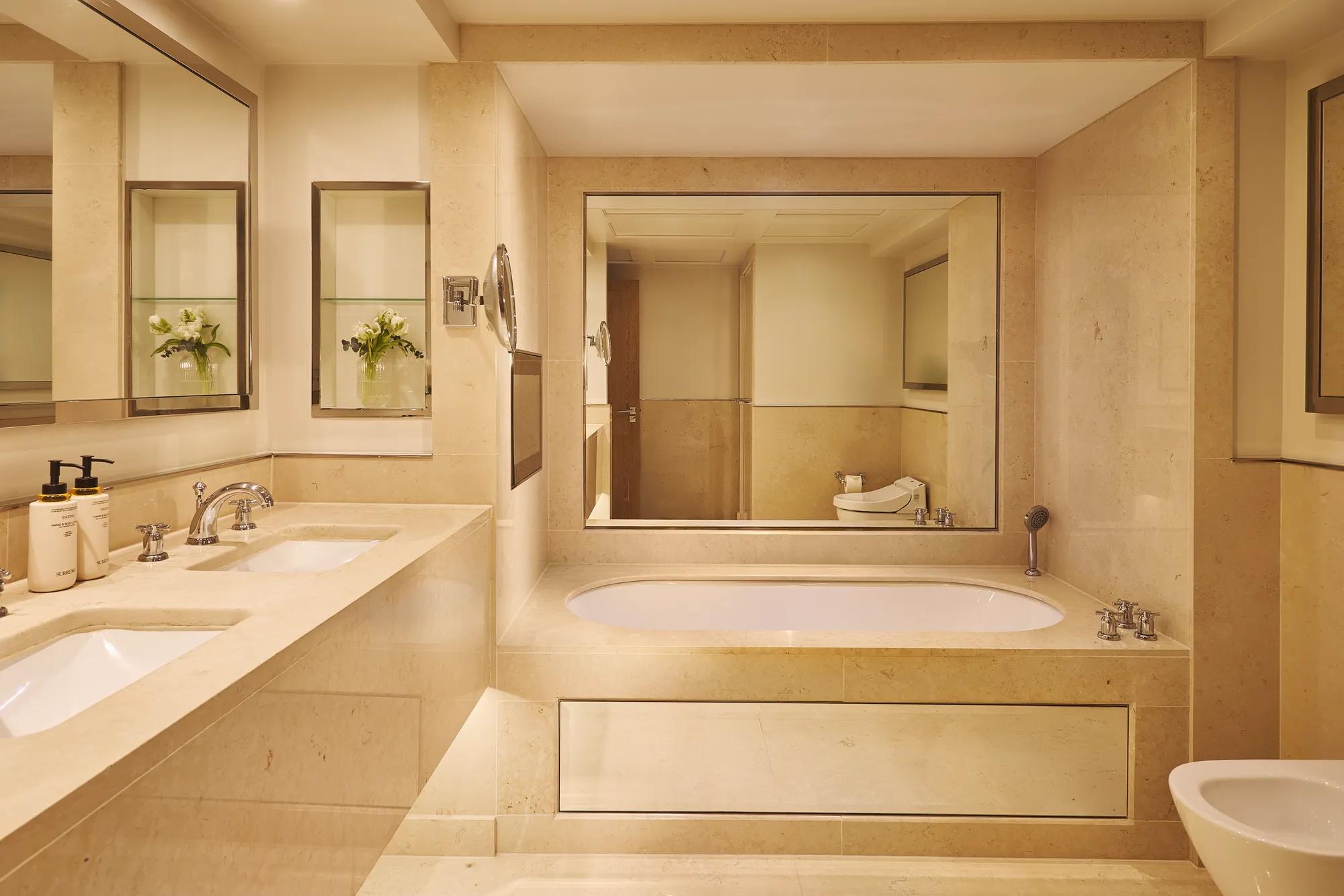 Marble bathroom with double sinks, built-in bathtub, large mirror, and separate bidet.