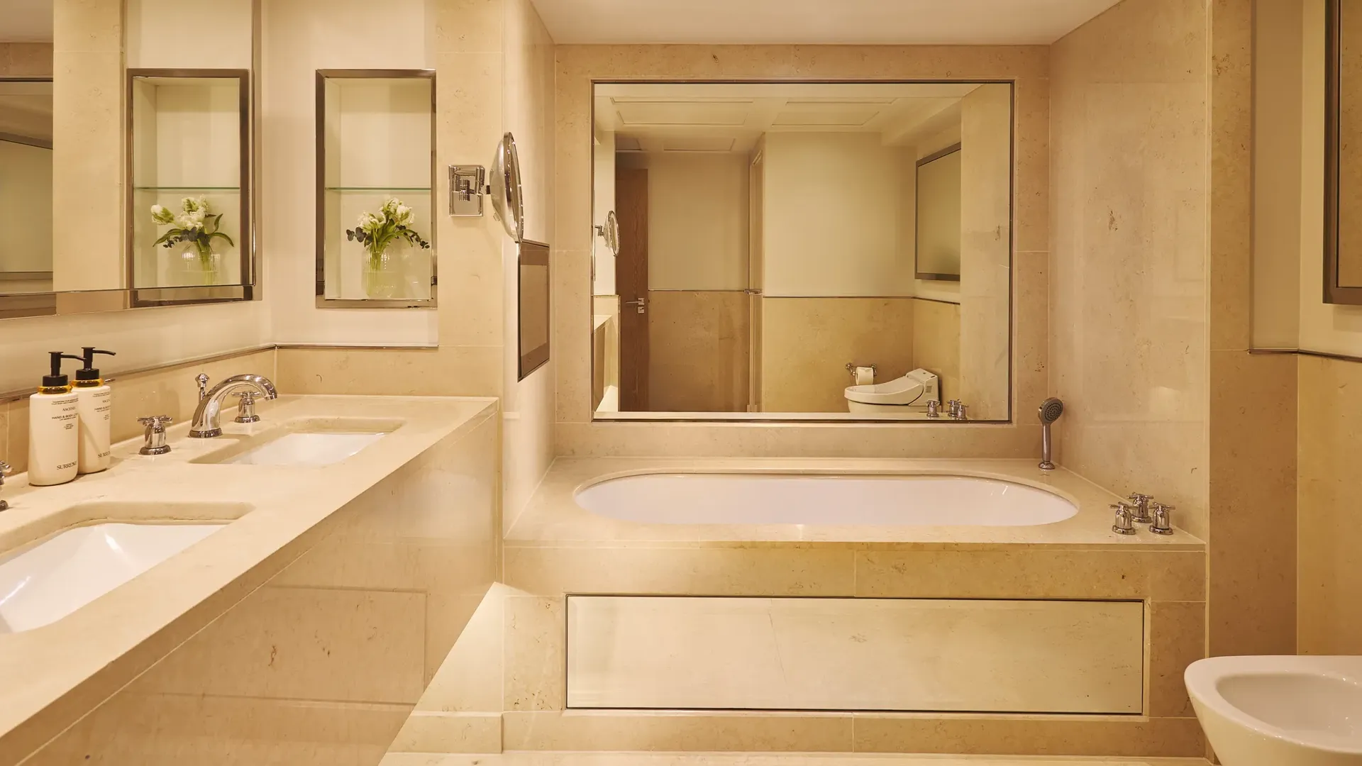 Marble bathroom with double sinks, built-in bathtub, large mirror, and separate bidet.