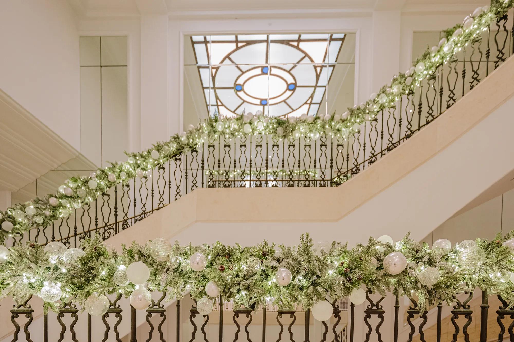 Grand staircase draped with garlands and ornaments under stained glass ceiling at Maybourne Beverly Hills.