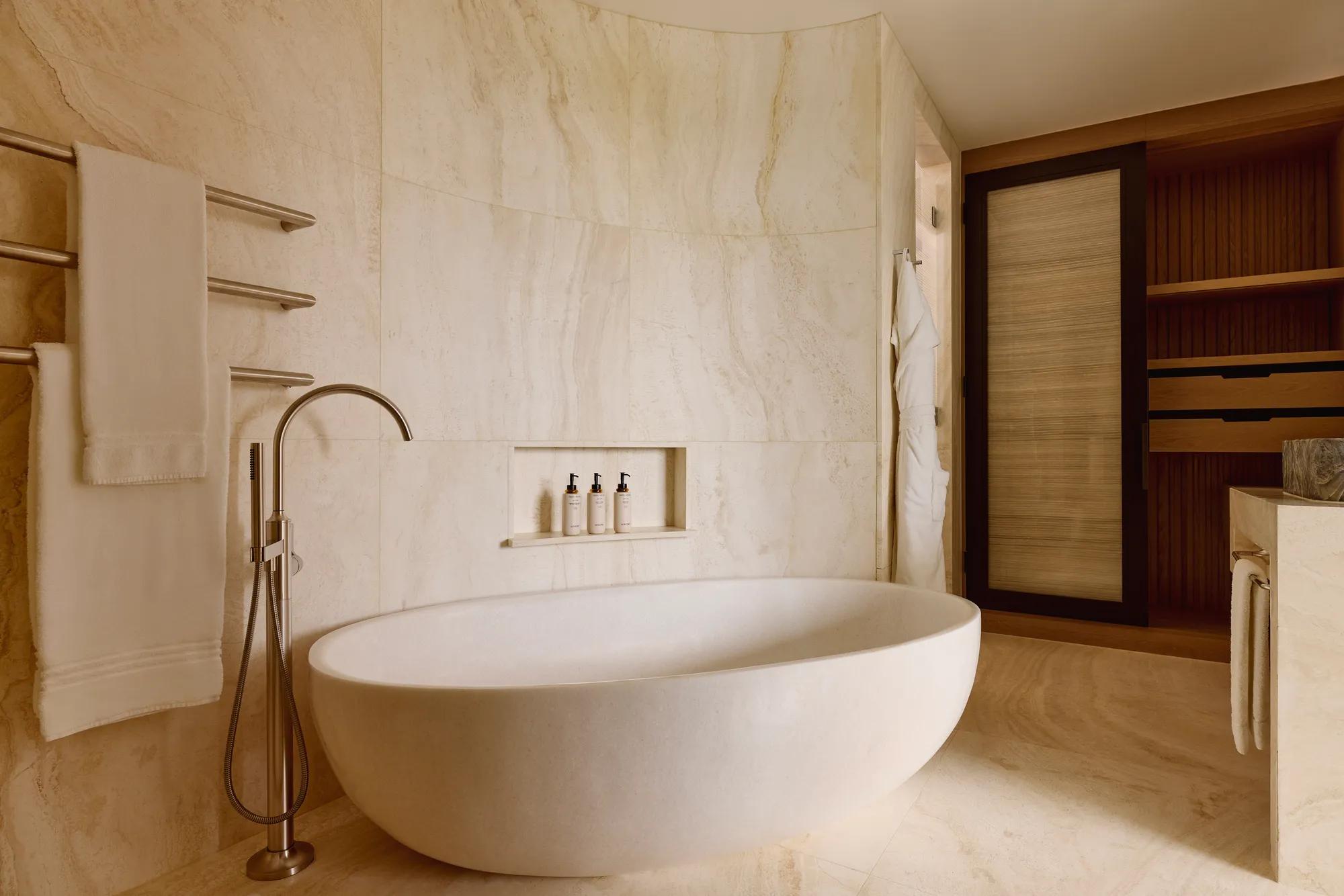 Luxurious bathroom with a freestanding oval bathtub, wall-mounted towels, built-in toiletries shelf, and wooden storage units.