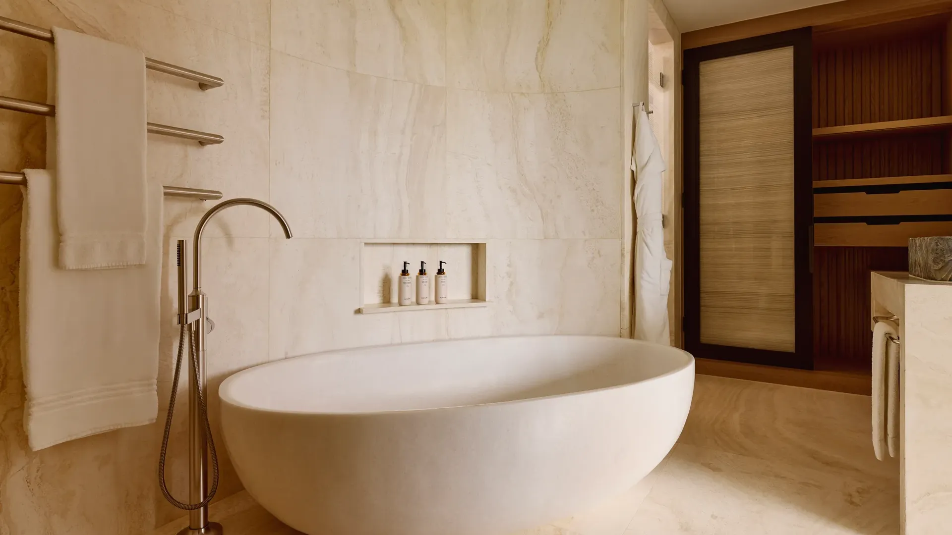 Luxurious bathroom with a freestanding oval bathtub, wall-mounted towels, built-in toiletries shelf, and wooden storage units.