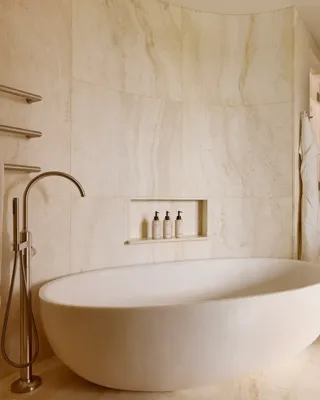 Luxurious bathroom with a freestanding oval bathtub, wall-mounted towels, built-in toiletries shelf, and wooden storage units.