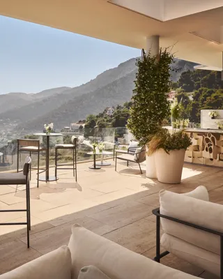 Terrasse élégante sur le toit avec tables de cocktail, bar, fleurs et vue panoramique sur montagnes et côte.