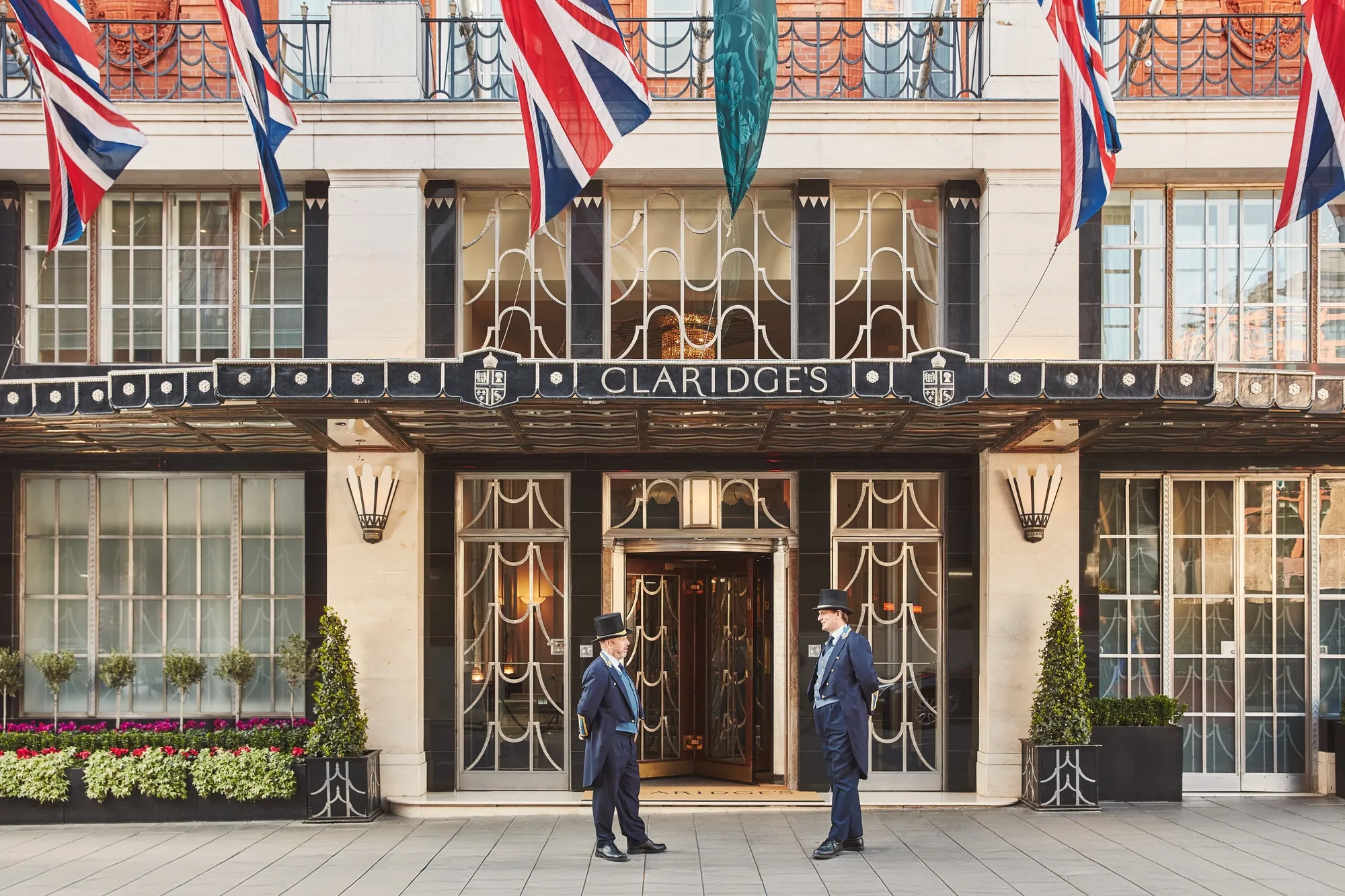 Claridge’s hotel entrance with Union Jack flags above the canopy and two uniformed doormen standing outside the doors.
