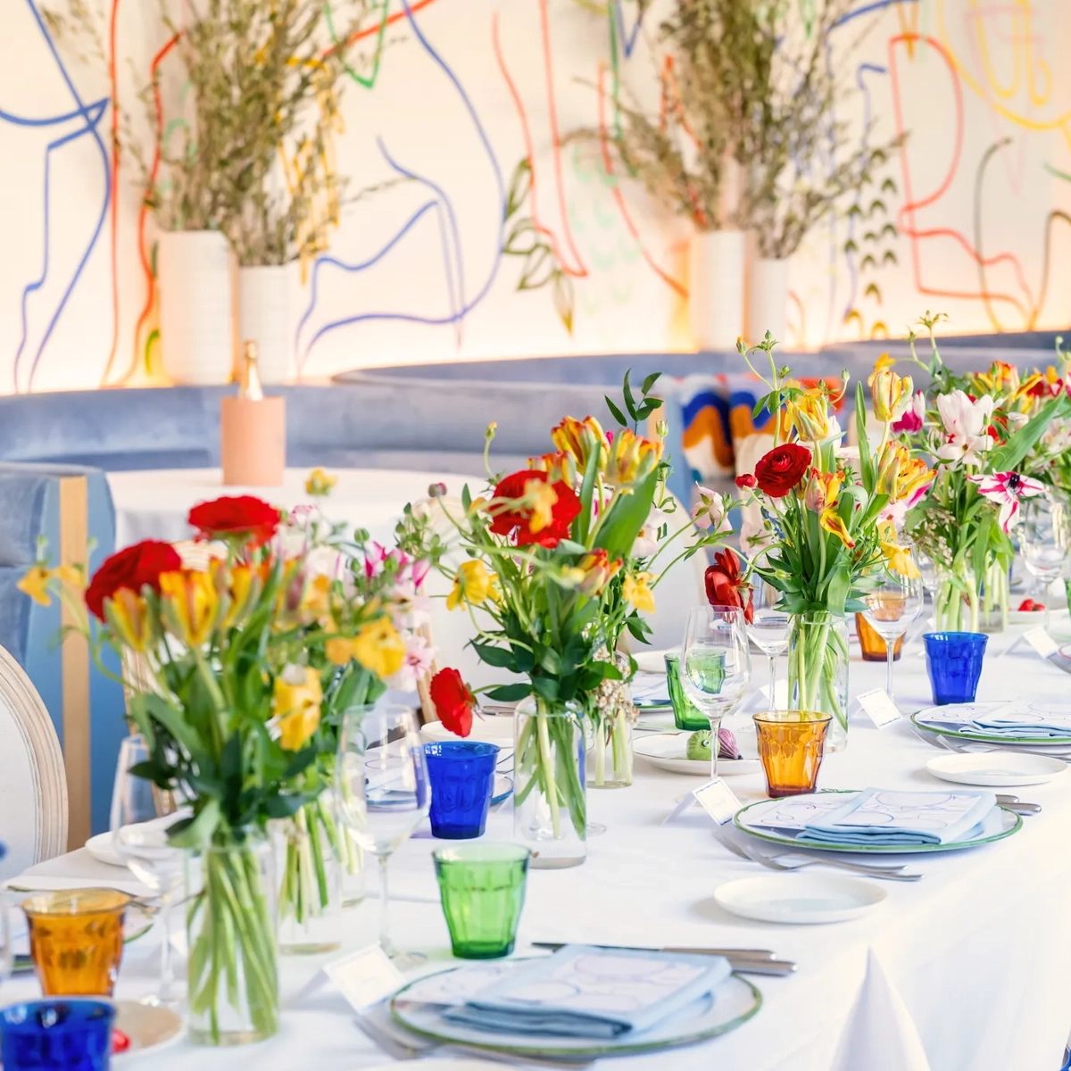 Long dining table on an indoor terrace in Beverly Hills, set with white linens and fresh flowers.