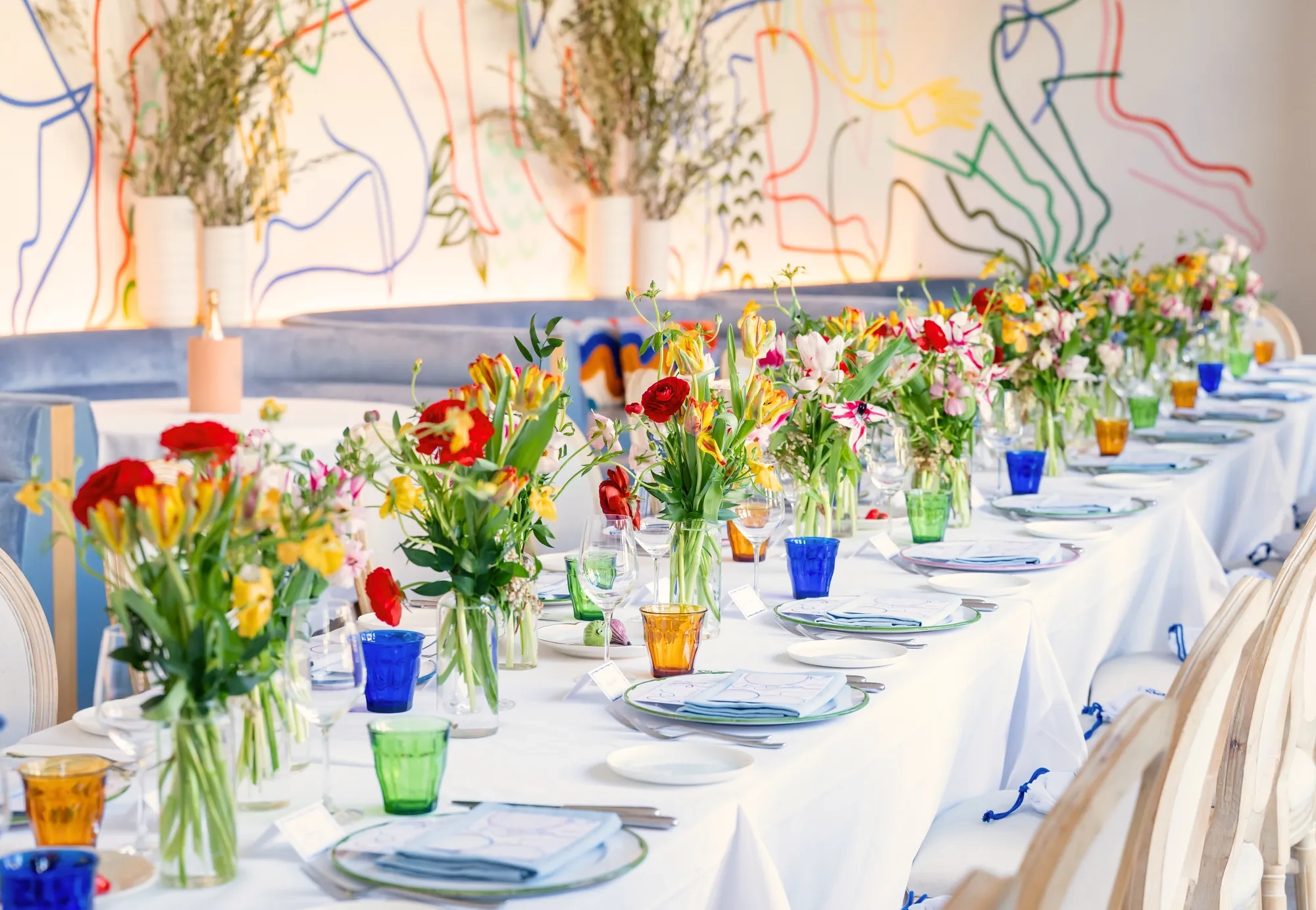 Long dining table on an indoor terrace in Beverly Hills, set with white linens and fresh flowers.