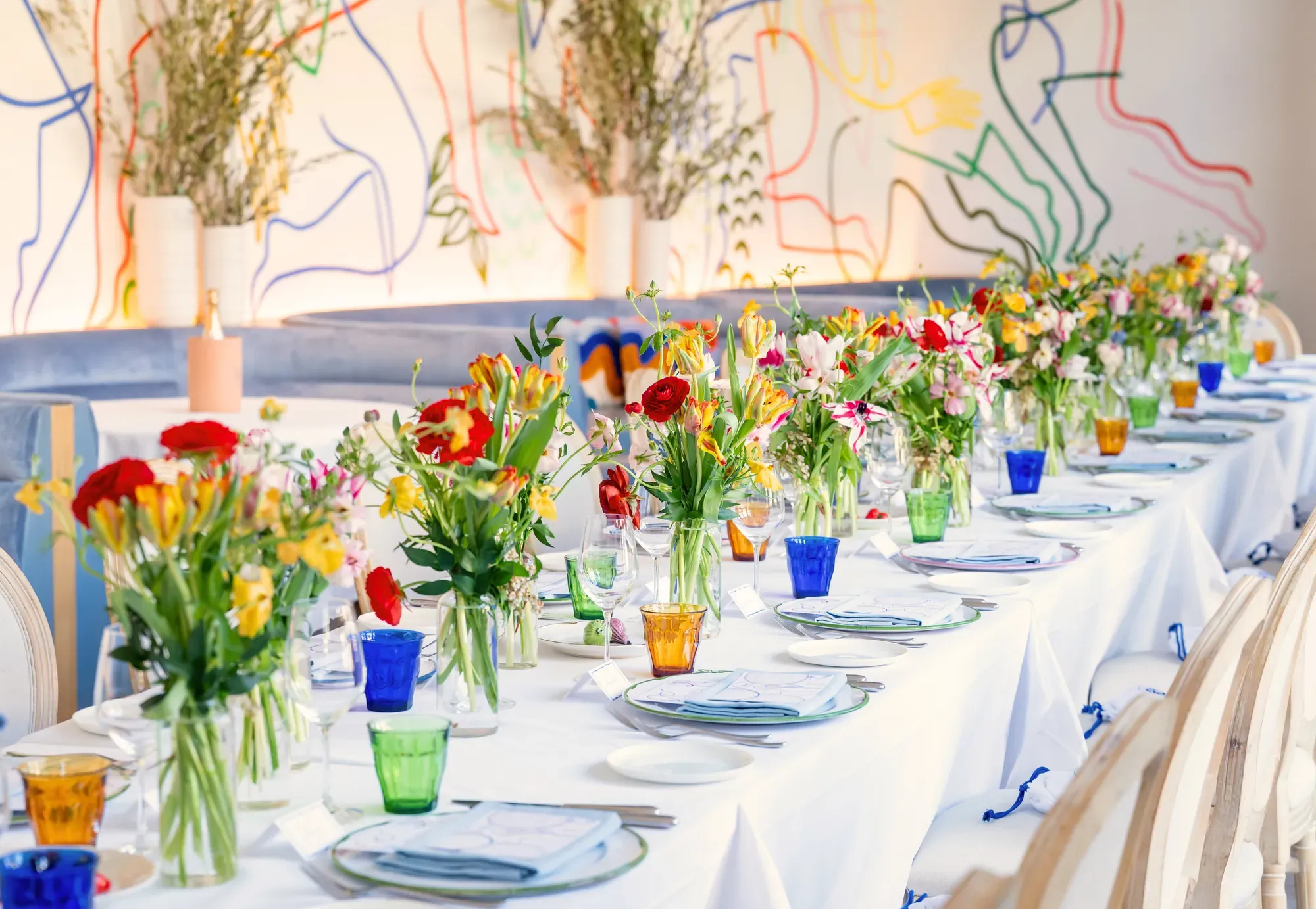 Long dining table on an indoor terrace in Beverly Hills, set with white linens and fresh flowers.