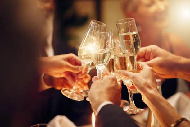 Guests raise champagne glasses in a festive toast, illuminated by warm candlelight during a celebratory gathering.