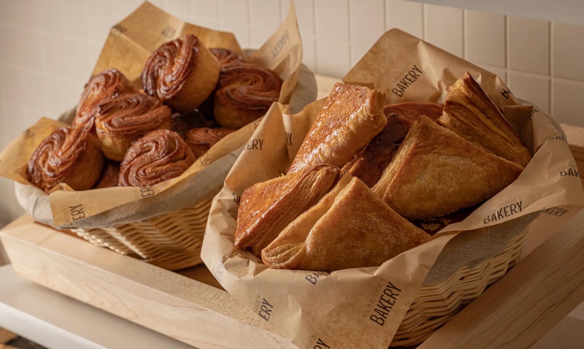 Baskets of pastries lined with paper, including laminated squares and spiral buns, displayed on wooden counter in bakery.