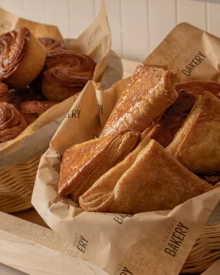 Baskets of pastries lined with paper, including laminated squares and spiral buns, displayed on wooden counter in bakery.