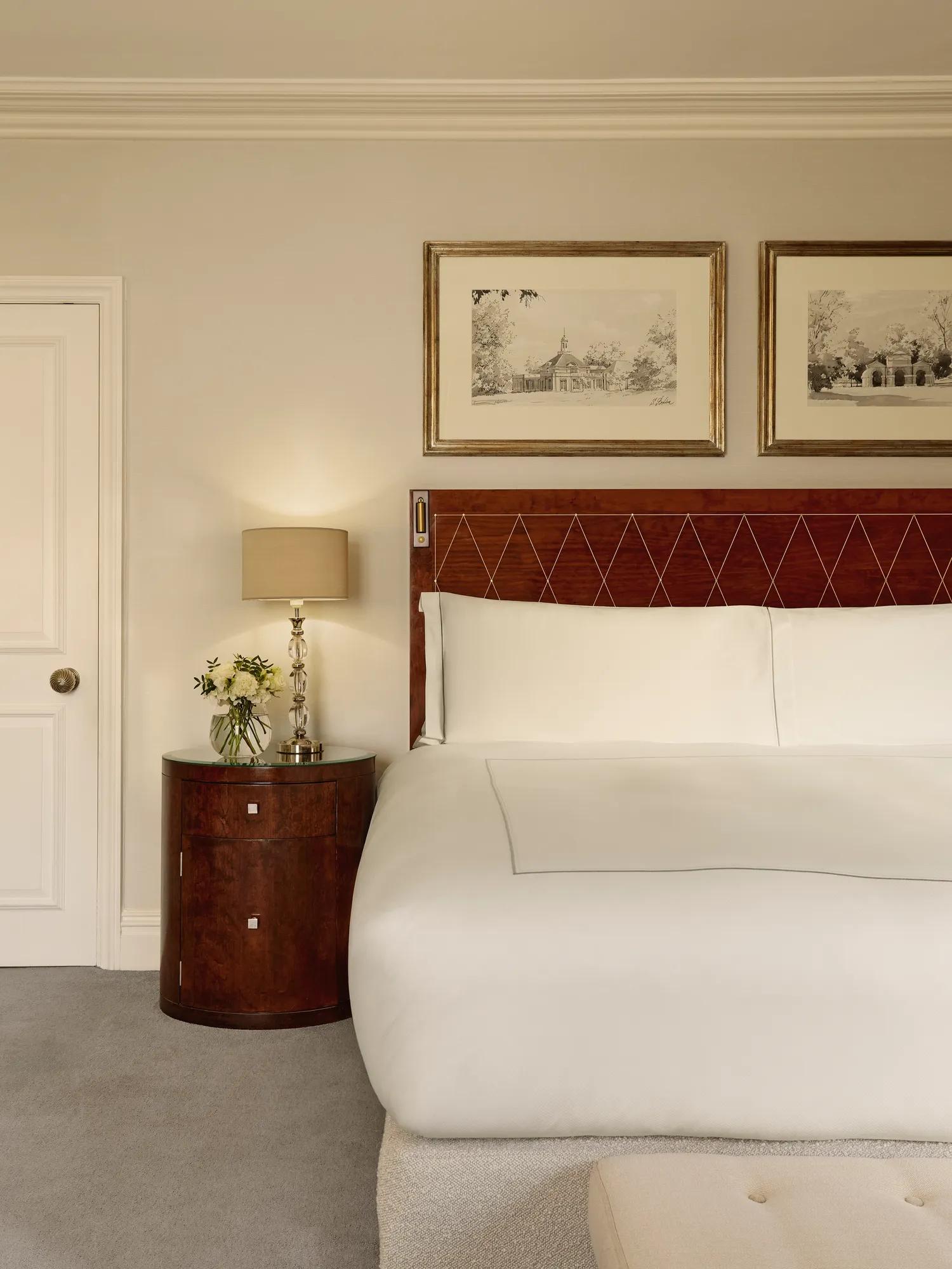Close-up of a king-size bed with a diamond-pattern wooden headboard, bedside table with fresh flowers, and framed artwork above.