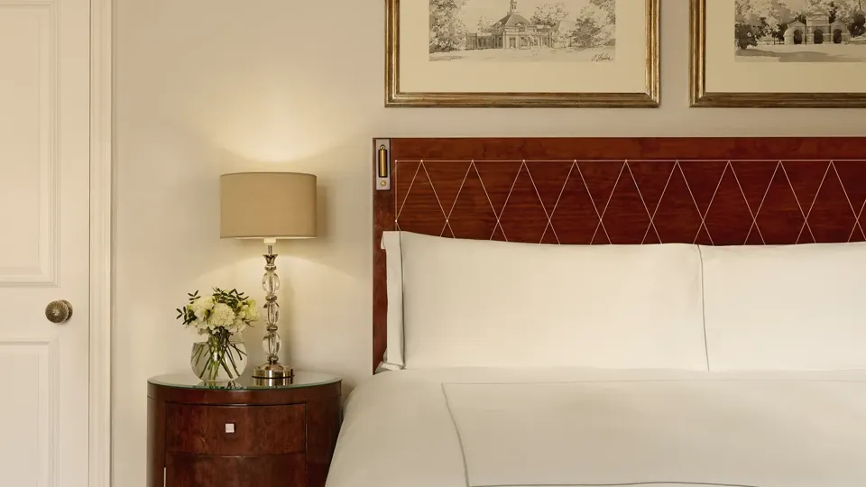 Close-up of a king-size bed with a diamond-pattern wooden headboard, bedside table with fresh flowers, and framed artwork above.