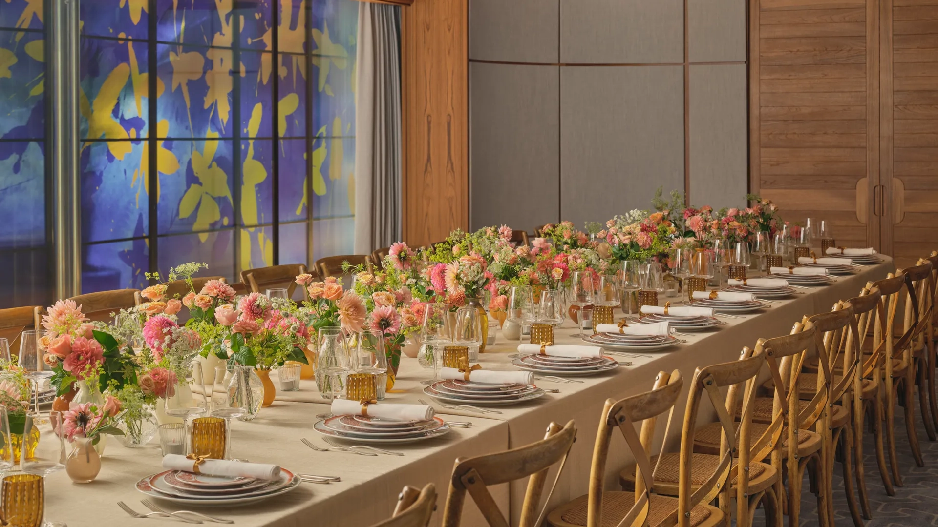 Long dining table set for an event, decorated with pink and peach flowers and glowing amber glassware