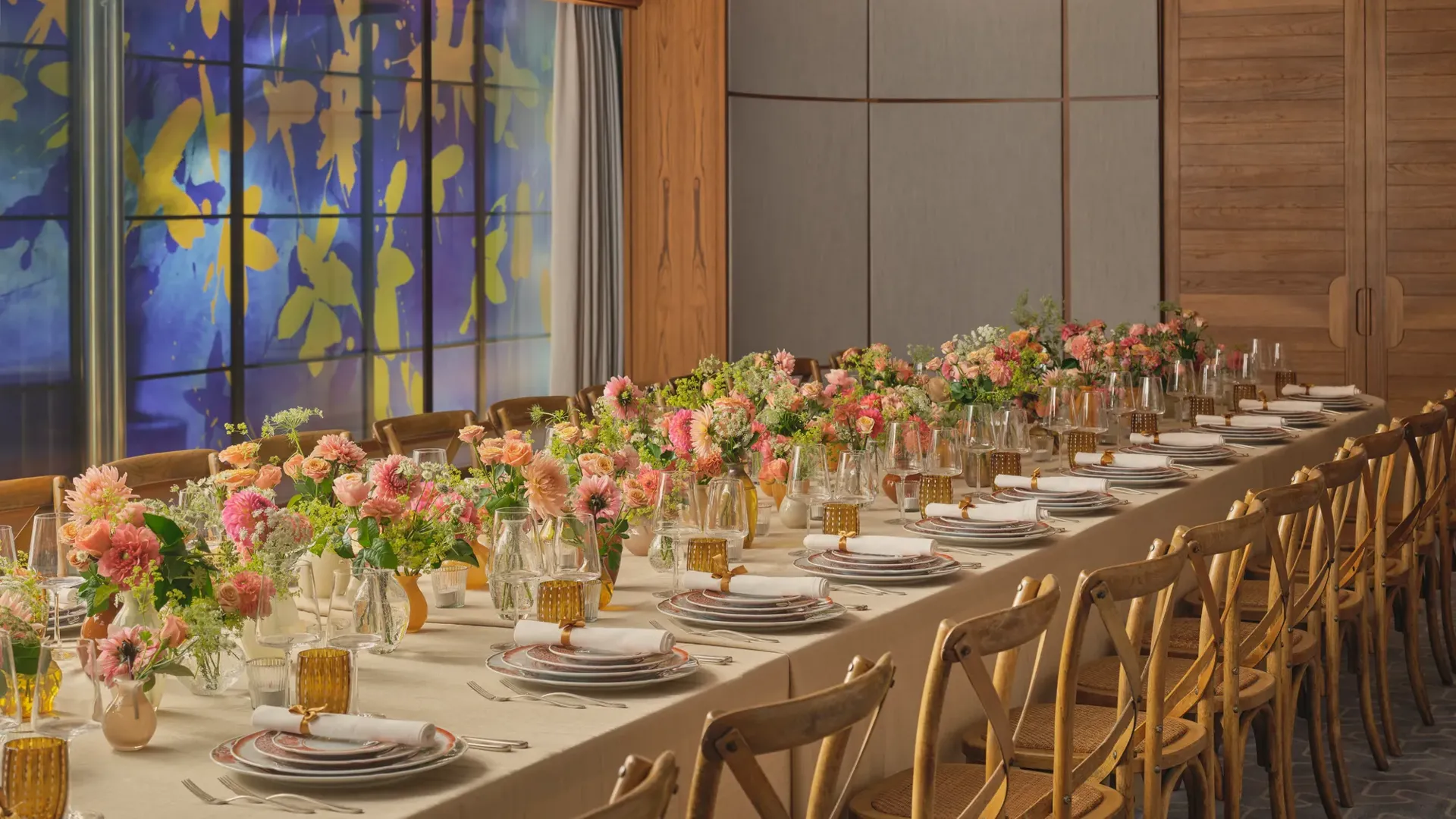 Long dining table set for an event, decorated with pink and peach flowers and glowing amber glassware