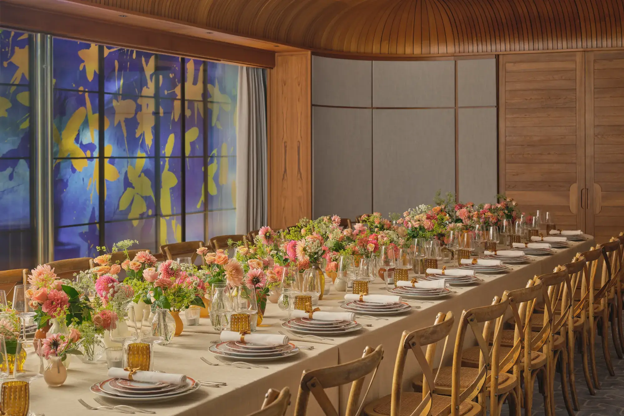 Long dining table set for an event, decorated with pink and peach flowers and glowing amber glassware
