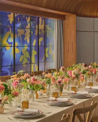 Long dining table set for an event, decorated with pink and peach flowers and glowing amber glassware