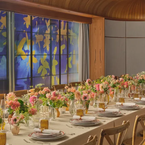 Long dining table set for an event, decorated with pink and peach flowers and glowing amber glassware