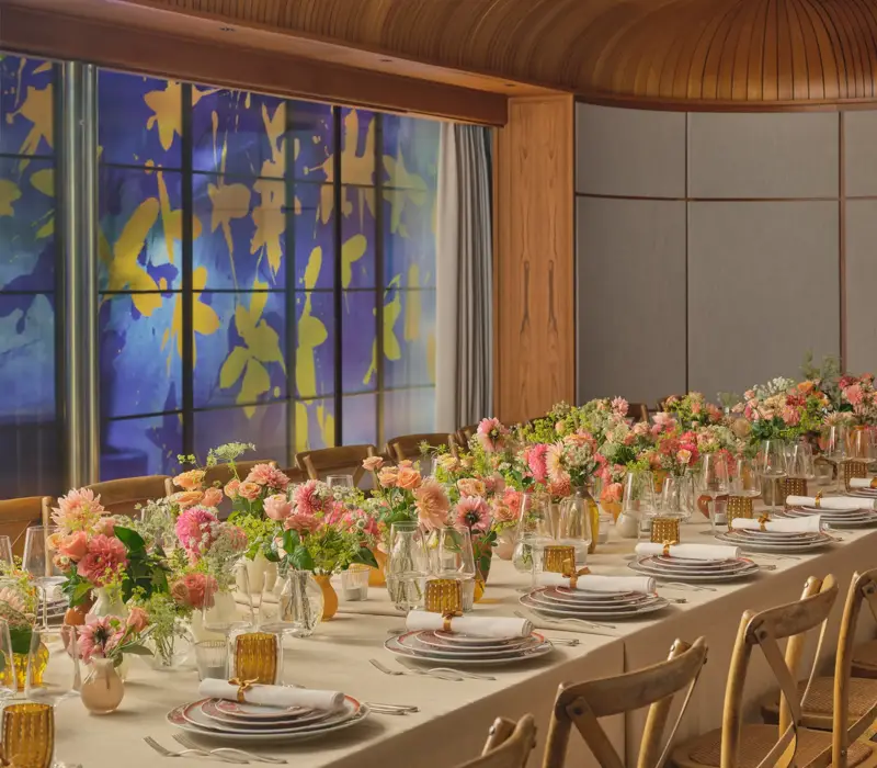 Long dining table set for an event, decorated with pink and peach flowers and glowing amber glassware
