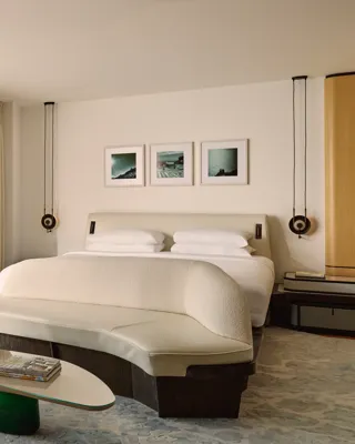 Stylish hotel bedroom with large bed, curved bench, and glass doors opening to a terrace with lounger, parasol, and mountain views.
