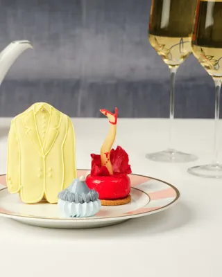 A yellow suit cookie, red leg pastry, and blue meringue treat on a plate with striped tea china behind.