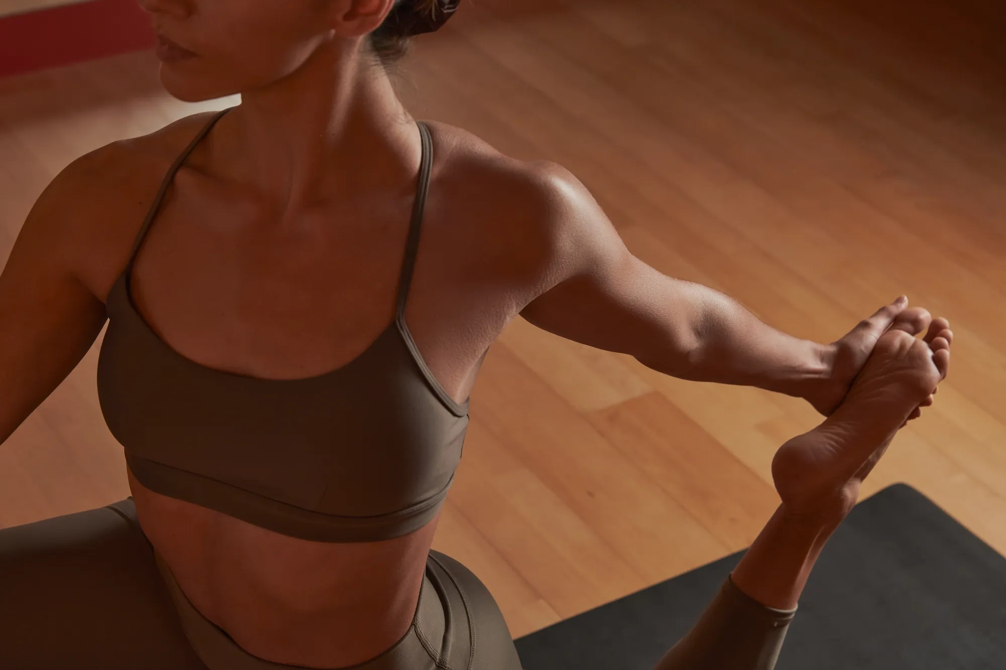 Person performing a seated yoga stretch on a mat, focusing on balance and flexibility in a studio setting.