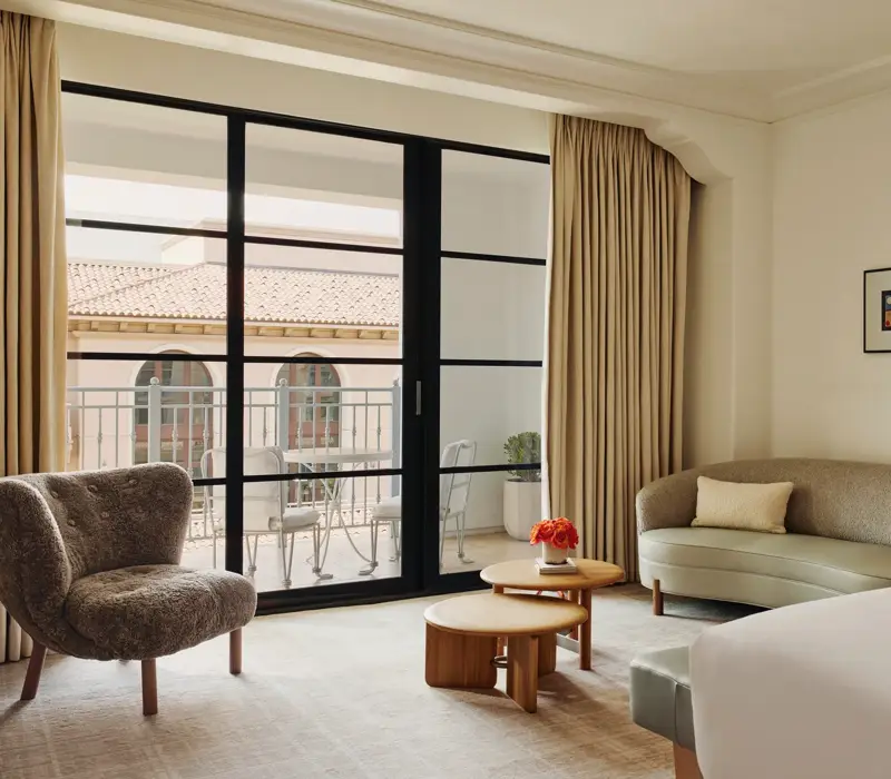 Sitting area with curved sofa, shearling lounge chair, nested round coffee tables, and sliding doors to a balcony with a small bistro set.