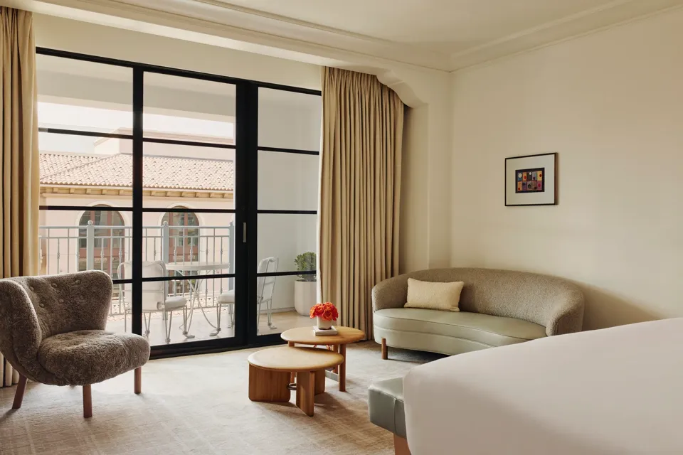 Sitting area with curved sofa, shearling lounge chair, nested round coffee tables, and sliding doors to a balcony with a small bistro set.