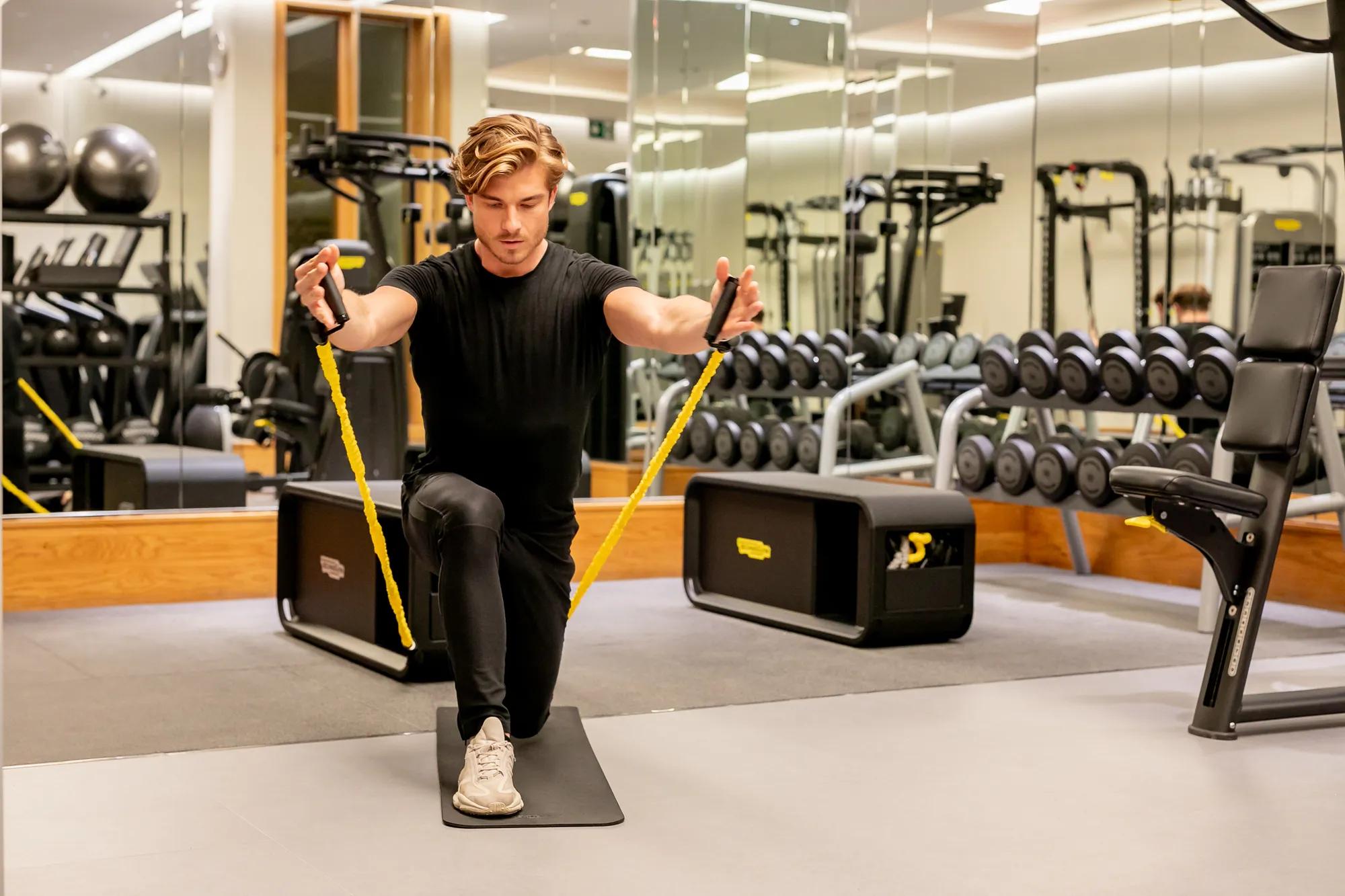 Man kneeling on a gym mat using yellow resistance bands for an upper-body exercise.
