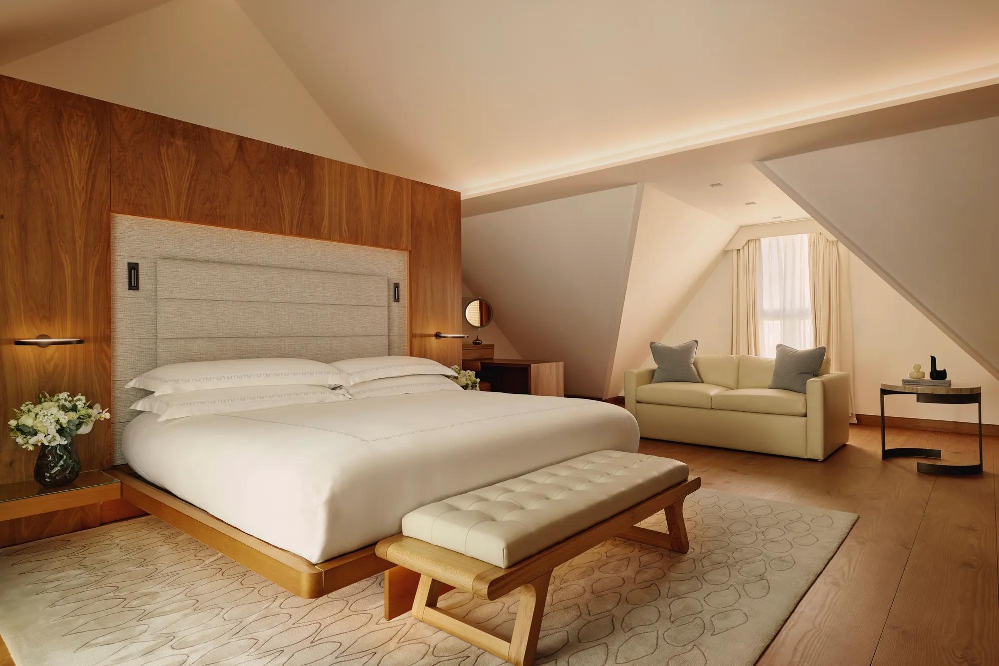 Serene attic bedroom with wooden feature wall, upholstered bed, cream sofa, and bench on a soft rug.