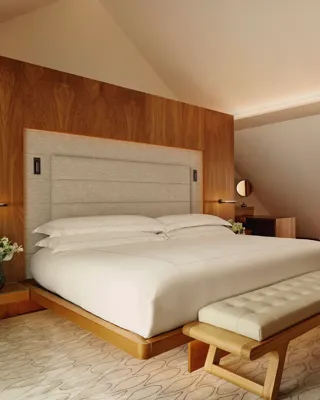 Serene attic bedroom with wooden feature wall, upholstered bed, cream sofa, and bench on a soft rug.