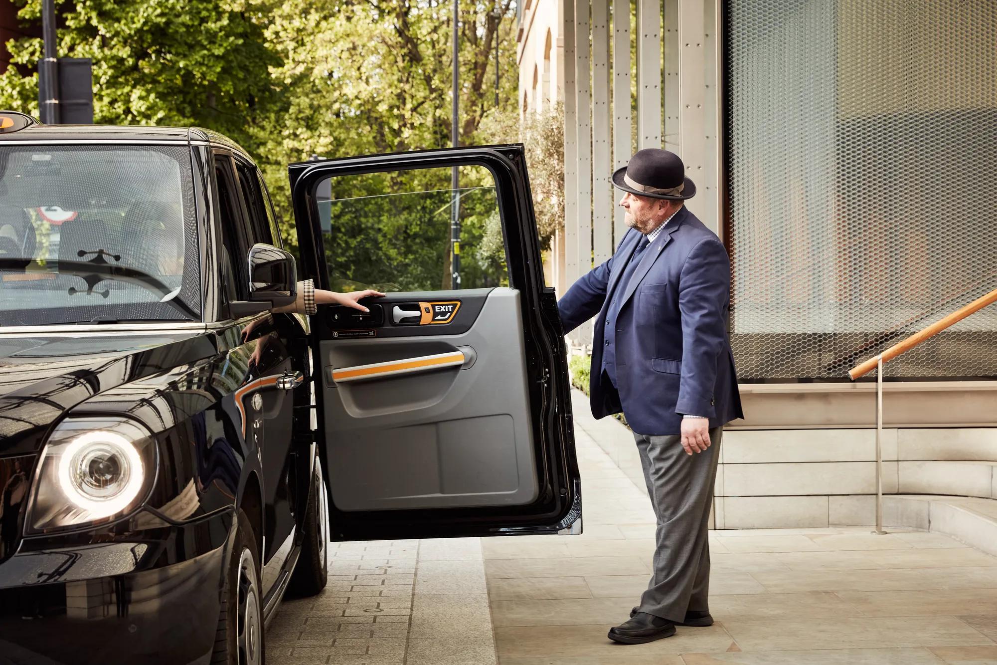 A doorman in a navy suit holds open the door of a black taxi as a guest steps out at the hotel entrance.