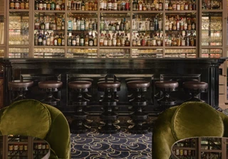 Elegant bar with a dark counter, high stools, mirrored shelves of spirits, and green velvet lounge chairs beneath a chandelier.